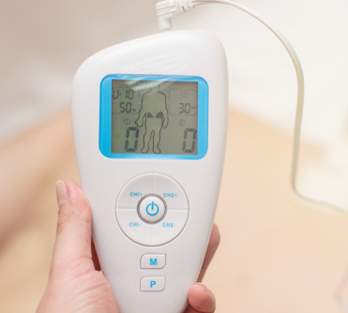 close-up of a doctor holding an electric muscle massager in the hand against a background of a blurred patient who has electrodes on his back