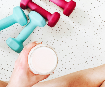 Top-down view photograph of a person holding a fitness beverage next to some free weights